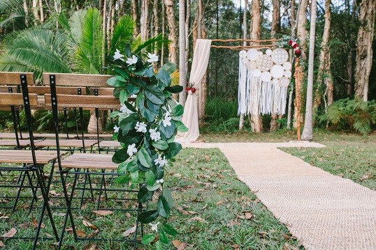Macrame ceremony backdrop with greenery and bench seating