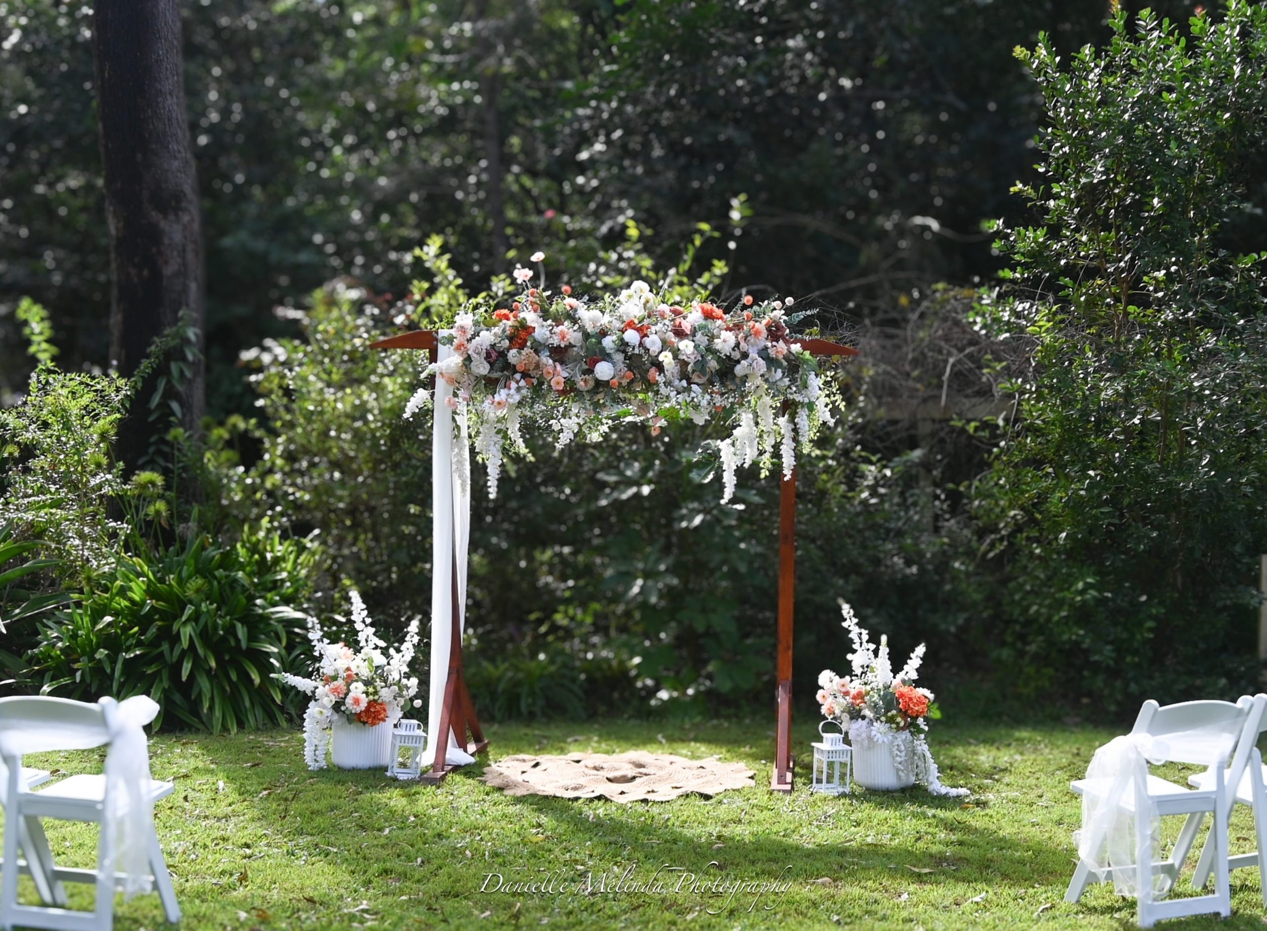 Wooden arbour dressed with flowers and draping on the garden lawn, white chairs either side